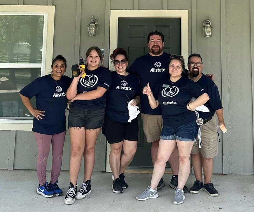 Group of volunteers smiling outside house.